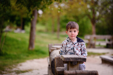 This image beautifully captures a pensive young boy sitting in a wooden structure at a park, surrounded by lush greenery. His contemplative gaze and the natural