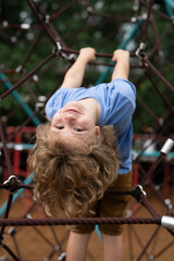 The child is hanging upside down on the playground equipment. Funny Child climbing outdoor....