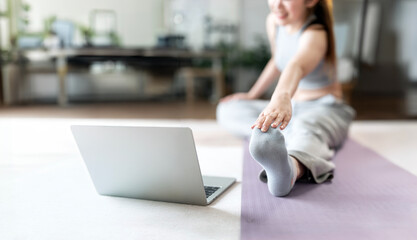 Fit woman doing exercise and watching online tutorials on laptop, training in living room