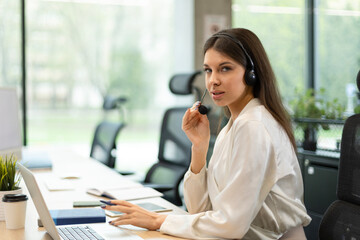 Obraz premium Cheerful female manager sitting at office desk and performing corporate tasks using wireless connection on digital gadgets