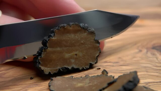 Hand cuts black truffle mushroom with a knife into a slices on a wooden board. High quality 4k footage