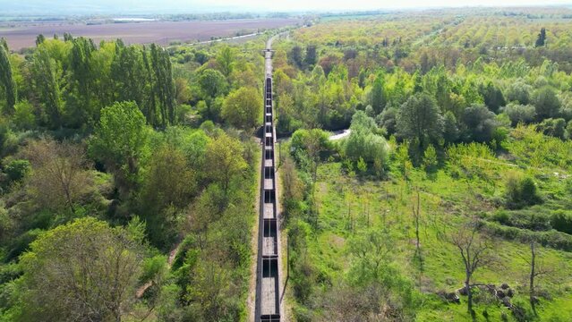 High angle tracking shot of an empty gondola long cargo train heading down to a mine to load up on materials. Drone flyover footage of a freight train heading for bulk load along a green summer day.
