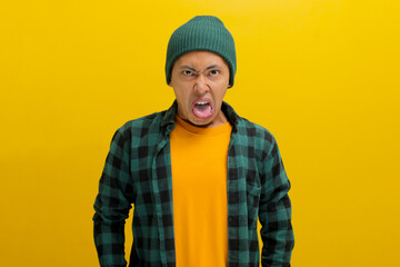 Displeased young Asian man, dressed in a beanie hat and casual shirt, is sticking out his tongue in...