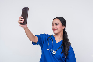 A young Asian female nursing aide dressed in blue scrub suit, happily taking a selfie with her...