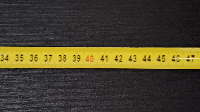 A yellow measuring tape is moving from right to left on a black background.