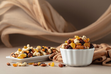 The mix of various nuts and raisins in a white bowl on a beige background.