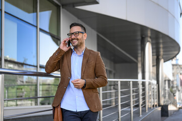 Smiling male professional looking away and sharing ideas over phone call outside building in city