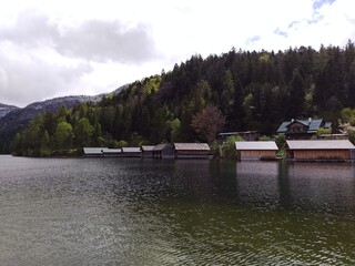 Beautiful traditional wooden boathouses at lake Altaussee in the Austrian Alps. Cloudy spring day. Green trees, snowy hills. Calming scenery in the countryside.