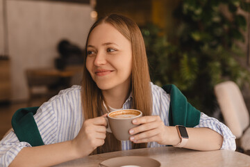 Close-up of laughing blonde girl wear shirt with coffee in coffee shop. Lovable lady sitting in...