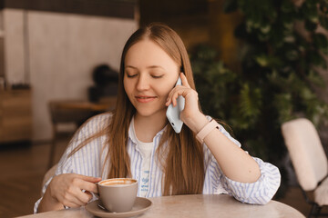 Blonde woman smiling positive conversation talking to her friend using phone hand hold hot drink coffee relax casual positive emotion weekend relax routine at cafe restaurant. Girl have discussion.