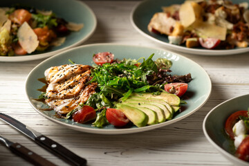 Plate with fried eel, avocado slices and arugula served on the table with other dishes for dinner in a restaurant