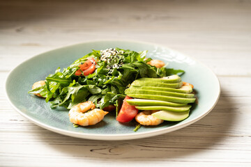 Fresh shrimp salad with tomato, arugula, avocado and spices. Seafood caesar salad in a blue plate