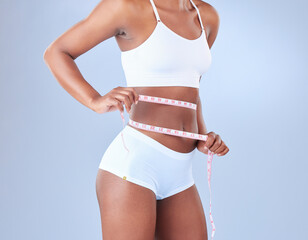 Woman, waist and weight loss with tape measure in underwear on a blue studio background. African,...