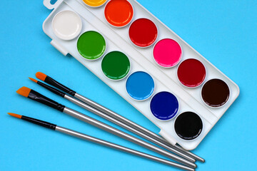 paint brushes and watercolor paints on a blue background. the concept of back to school