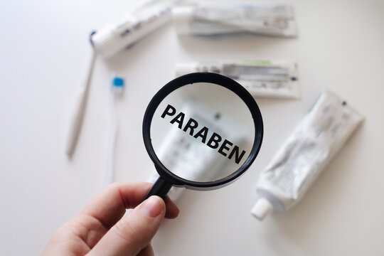 Dangerous toothpaste ingredient Paraben. Checking the composition of toothpaste with a magnifying glass against the background of many tubes