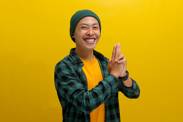 Excited Asian man, dressed in a beanie hat and casual shirt, dances joyfully and makes a finger...
