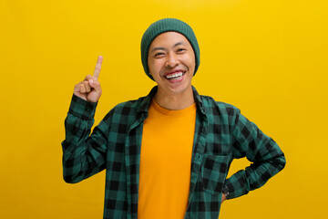 Excited young Asian man, dressed in a beanie hat and casual shirt, has an idea, raising his finger...