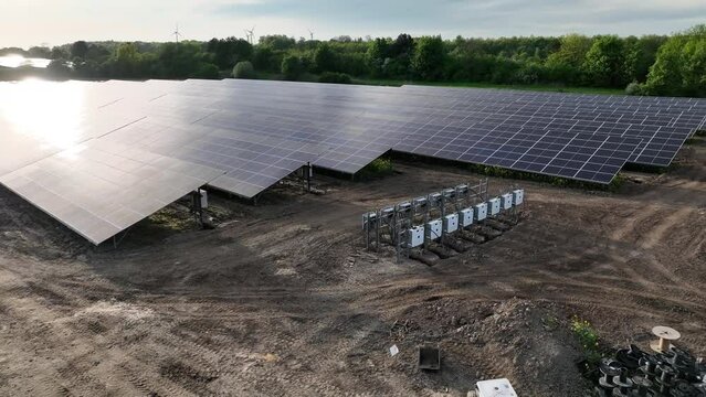 Shot of the industrial solar power station, currently under construction, showcasing solar modules and the array of white combiner boxes with power cables for connection to solar energy system grid.