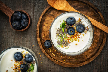 Still life homemade yogurt with blueberries, osmanthus flowers, chia seeds and pea sprouts on a wooden gray background with wooden utensils. View from above.