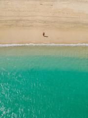 Aerial view of a girl in a swimsuit standing on the ocean shore near the tide of turquoise waves