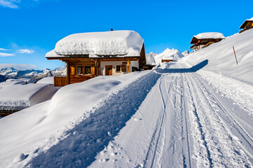Road in alpine village with traditional wooden houses in winter mountain snow landscape,...