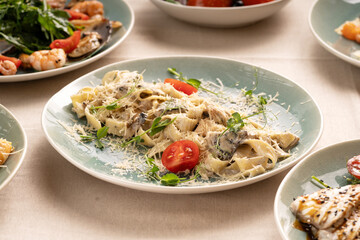 Pasta fettuccine with mushrooms and fried chicken meat in creamy cheese sauce garnished tomatoes on a light table in restaurant