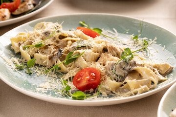 Pasta fettuccine with mushrooms and fried chicken meat in creamy sauce garnished tomatoes on a light table in restaurant