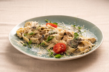 Traditional Italian fettuccine pasta with mushrooms and fried chicken in a creamy sauce with tomatoes on a plate