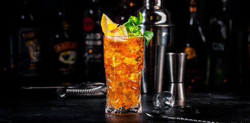 Boston ice tea, summer cocktail drink with rum, gin, vodka, tequila, liquor, juice, cola, lemon and ice in glass, dark bar background