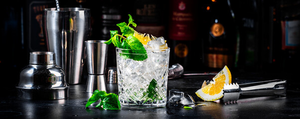 Summer refreshing drink cocktail with mint, lemon, vodka and gin tonic. Dark background bar counter, banner