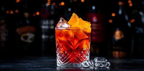 Coffee negroni red cocktail drink with dry gin, vermouth and bitter, espresso, liqueur, orange and ice. Black bar counter background