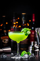 Summer green cocktail drink with gin, liqueur, lime, juice, mint and ice. Black bar counter...