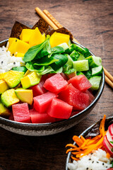Poke bowl with fresh tuna, avocado, mango, cucumber, lettuce and white rice. Soy sauce, lime and sesame dressing. Old rustic wooden table background, top view