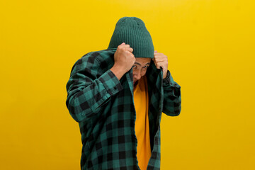 The amusingly frightened young Asian man hides his face with his shirt, expressing a mix of fear,...