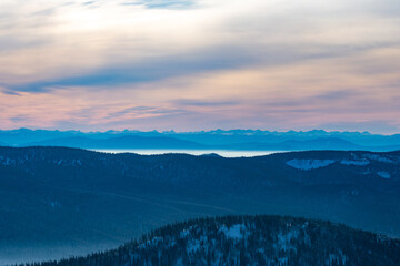 Mountain peaks in the dramatic orange light of the rising sun with fog and forested mountains
