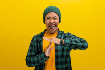 Furious Asian man in beanie and casual shirt holds up a hand in a TIME OUT gesture, yelling towards the camera with a frustrated expression. Frustration, disagreement, and demanding attention concept