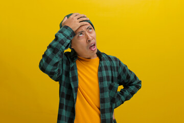 Troubled young Asian man, dressed in a beanie hat and casual shirt, is depicted holding his hand to...