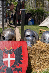 A group of medieval helmets and a shield are displayed in a field. The helmets are arranged in a...