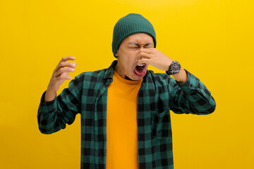 Young Asian man, dressed in a beanie hat and casual shirt, is pinching his nose with his fingers,...