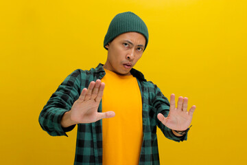 An afraid young Asian man, dressed in a beanie hat and casual shirt, is pulling his hands away with...