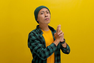 Young Asian man, dressed in a beanie hat and casual shirt, makes a finger gun gesture, mimicking...