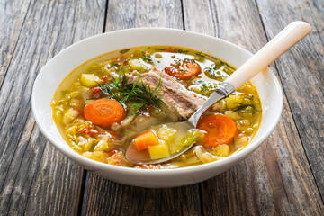 Cabbage soup with pork ribs served in white bowl on wooden table
