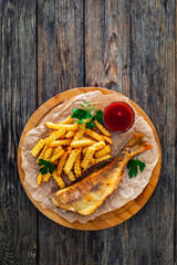 Fried sea bass served on paper with French fries and ketchup on board on wooden table 