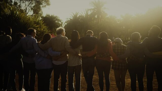 Back view of happy multigenerational people having fun in a public park during sunset time