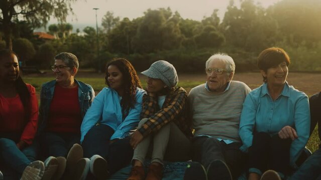 Happy multi generational people having fun sitting on grass in a public park - Diversity and friendship concept