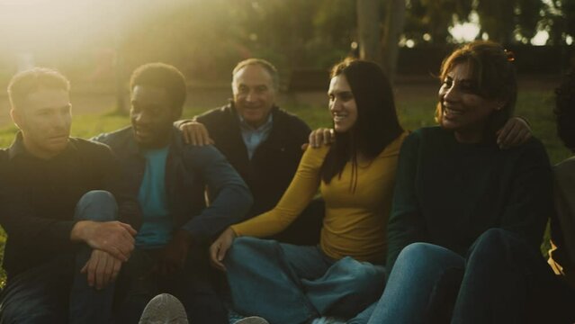 Happy multi generational people having fun sitting on the grass in a public park - Diversity and friendship concept
