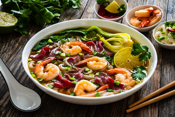 Shrimp and beef Pho soup - Vietnamese soup with shrimps and raw beef slices on wooden table
