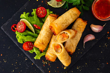 Spring rolls filled with cooked vegetables served with  sauces on wooden table
