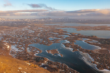 Winter frozen lakes on swamps on mountain hills under cloudy sunset. Iceland, north-eastern region.