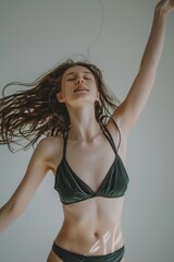 A young woman in a swimsuit dancing on a white background, capturing a moment of joyful motion. - obrazy, fototapety, plakaty